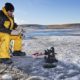 man-ice-fishing-on-frozen-canadian | Ice Fishing Gear Checklist For The Winter Fishermen | Featured