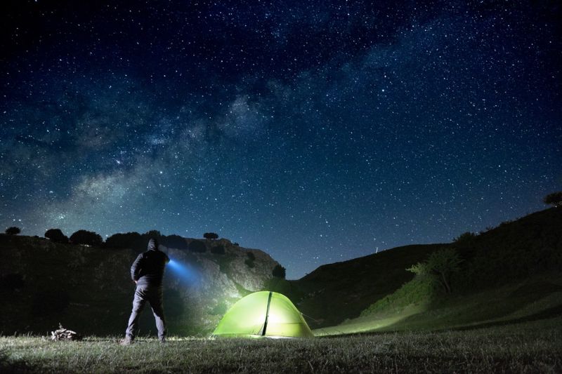man-pointing-blue-flashlight-mountain-below | camping at night