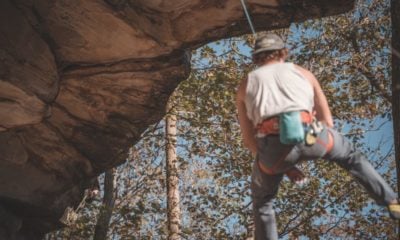 man in white tank top and blue denim jeans climbing on brown | Stay Safe: Why You Should Bother With Rock Climbing Insurance | Featured