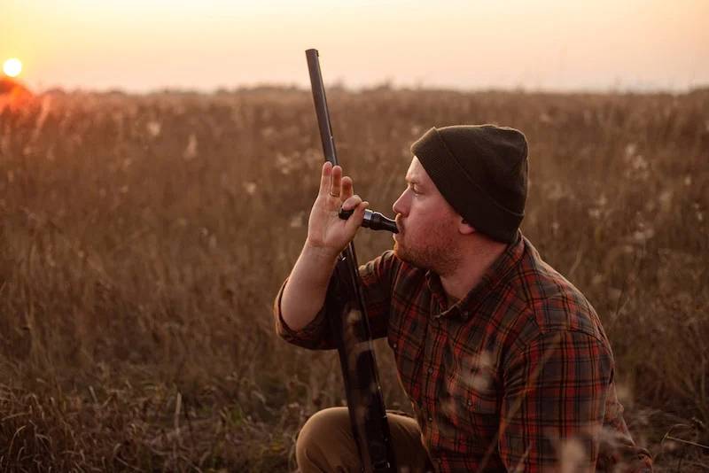 Young red bearded hunter sitting it grass and blowing at hunter's whistle | essential hunting clothes