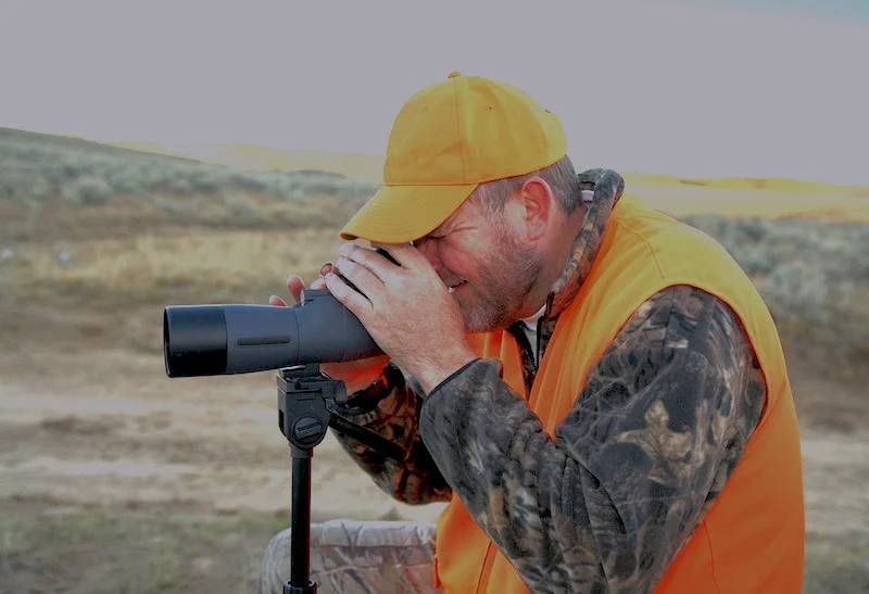 hunter wearing orange and looking through spotting scope | coyote hunting at night in missouri