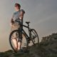 Young Man in Shorts with Hybrid Mountain bike on a rocky hill | How To Buy the Best Hybrid Bike | featured