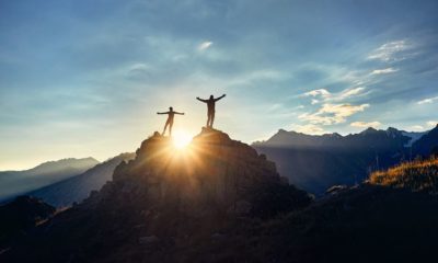 two-hikers-silhouette-stands-on-rock | Climbing A Mountain And The Dangers Of It | The Outside Podcast [LISTEN] | Featured